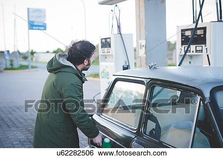Stock Photograph - Man using fuel pump for vintage car in gas filling station. Fotosearch