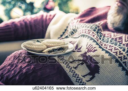 Stock Photography - Man wearing sweater asleep with mince pies on chest. Fotosearch