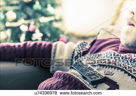 Stock Photo - Man wearing sweater asleep with remote control on chest. Fotosearch