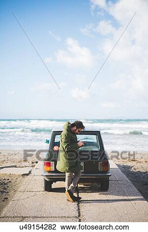 "Man with vintage car parked on beach reading smartphone texts, Sorso, Sassari, Sardinia, Italy" View Large Photo Image Stock Image - "Man with vintage car parked on beach reading smartphone texts, Sorso, Sassari, Sardinia, Italy". Fotosearch