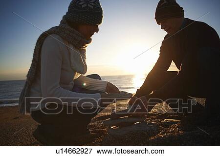 Mature couple stacking stones on beach at dusk View Large Photo Image Stock Photo - Mature couple stacking stones on beach at dusk. Fotosearch