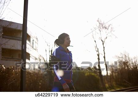 Stock Photo - Mature female runner in park listening to music on headphones. Fotosearch