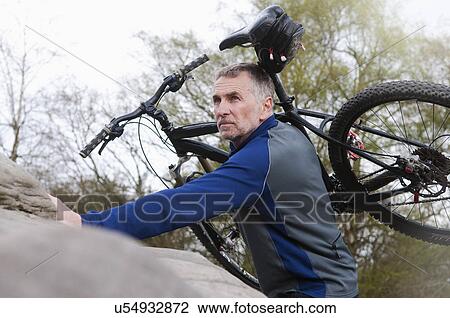 Mature male mountain biker carrying bike over rock formation View Large Photo Image Stock Image - Mature male mountain biker carrying bike over rock formation. Fotosearch