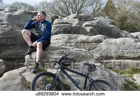 Picture - Mature male mountain sitting on rock formation. Fotosearch