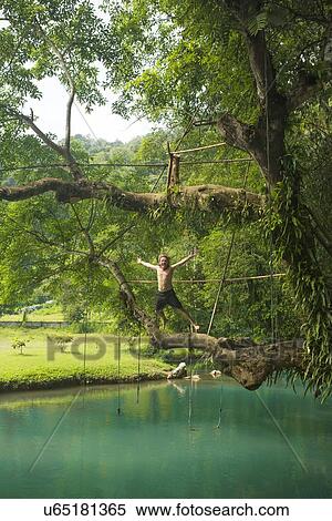 Stock Photography - "Mature man jumping mid air into turquoise lagoon, Vang Vieng, Laos". Fotosearch