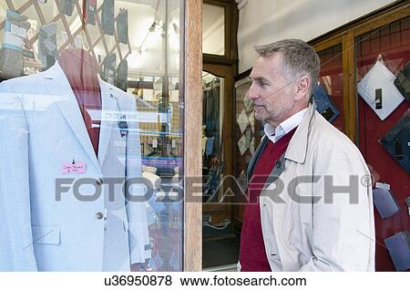 Stock Photo - Mature man looking at suit jacket in tailors shop window. Fotosearch