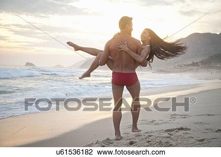"Mid adult couple on beach, man carrying woman in arms, rear view" View Large Photo Image Stock Image - "Mid adult couple on beach, man carrying woman in arms, rear view". Fotosearch