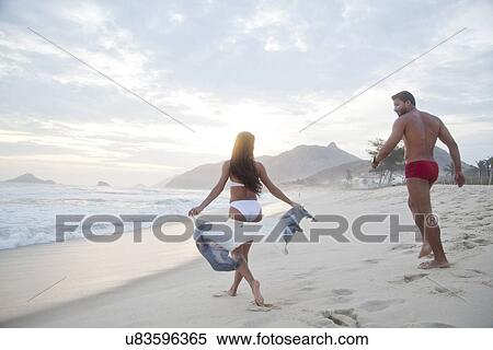 Stock Photography - "Mid adult couple on beach, walking towards ocean, rear view". Fotosearch