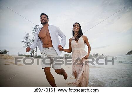 "Mid adult couple running along beach, hand in hand, low angle view" View Large Photo Image Stock Image - "Mid adult couple running along beach, hand in hand, low angle view". Fotosearch