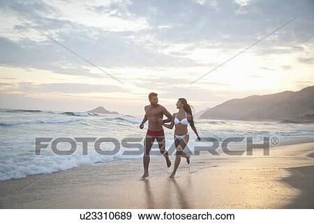 "Mid adult couple running along beach, hand in hand" View Large Photo Image Stock Photo - "Mid adult couple running along beach, hand in hand". Fotosearch