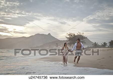 "Mid adult couple running along beach, hand in hand" View Large Photo Image Stock Photograph - "Mid adult couple running along beach, hand in hand". Fotosearch