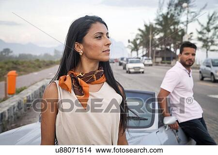 Mid adult couple standing by convertible car by side of road View Large Photo Image Picture - Mid adult couple standing by convertible car by side of road. Fotosearch