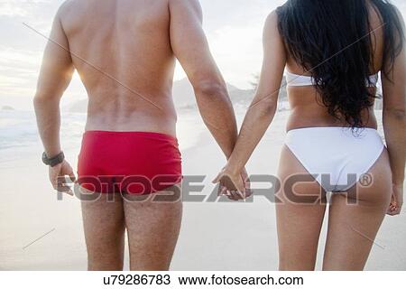 "Mid adult couple standing on beach, hand in hand, wearing swimwear, rear view" View Large Photo Image Stock Image - "Mid adult couple standing on beach, hand in hand, wearing swimwear, rear view". Fotosearch