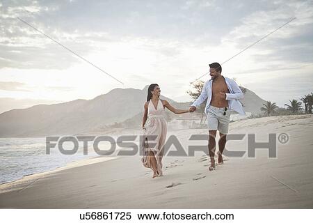 Stock Photography - "Mid adult couple walking along beach, hand in hand". Fotosearch