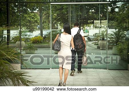 Stock Image - "Mid adult couple, walking into building, rear view". Fotosearch