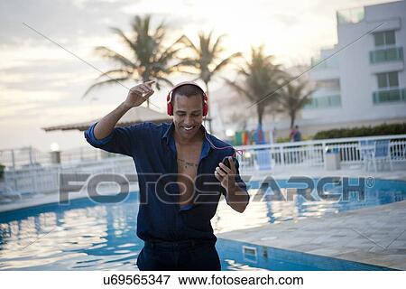 Stock Photo - "Mid adult man dancing to smartphone music at hotel poolside, Rio De Janeiro, Brazil". Fotosearch