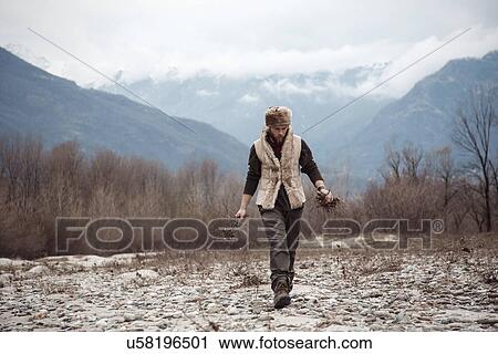 Stock Image - Mid adult man gathering firewood. Fotosearch