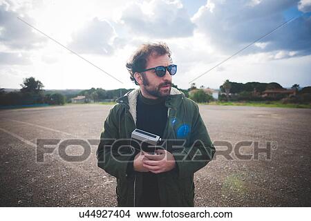 Mid adult man holding vintage movie camera on waste ground View Large Photo Image Picture - Mid adult man holding vintage movie camera on waste ground. Fotosearch