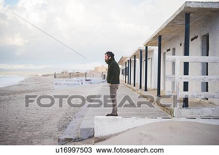 Stock Image - "Mid adult man in front of beach huts, Sorso, Sassari, Sardinia, Italy". Fotosearch