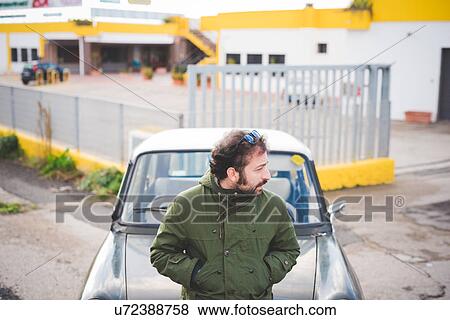 Stock Photo - Mid adult man leaning on vintage car looking over his shoulder. Fotosearch