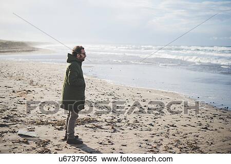 Stock Photography - "Mid adult man looking out at sea on windy beach, Sorso, Sassari, Sardinia, Italy". Fotosearch