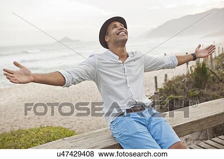 "Mid adult man sitting on boardwalk fence with arms open, Rio De Janeiro, Brazil" View Large Photo Image Stock Photo - "Mid adult man sitting on boardwalk fence with arms open, Rio De Janeiro, Brazil". Fotosearch