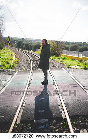 Stock Image - Mid adult man standing on railway crossing. Fotosearch