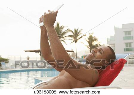 Stock Photography - "Mid adult man taking digital tablet selfie at hotel poolside, Rio De Janeiro, Brazil". Fotosearch