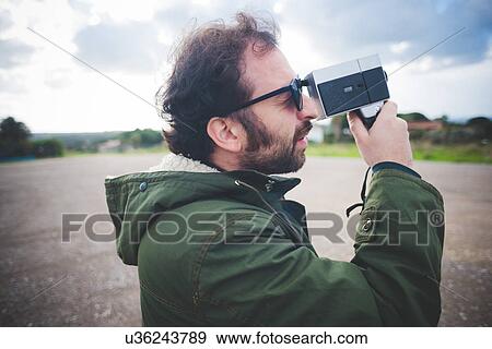 Stock Photo - Mid adult man using vintage movie camera on waste ground. Fotosearch