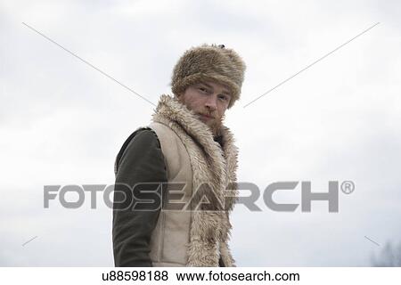 Stock Photo - Mid adult man wearing furry waistcoat and trapper hat. Fotosearch