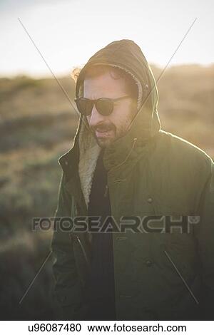 Stock Image - Mid adult man wearing hooded anorak in field. Fotosearch