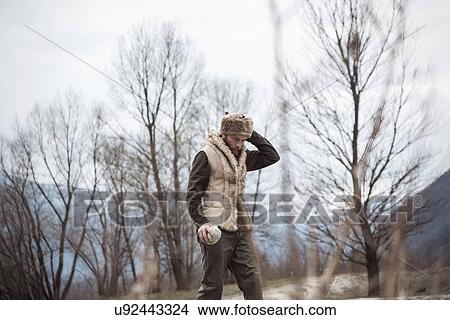 Mid adult man wearing trapper hat by trees View Large Photo Image Picture - Mid adult man wearing trapper hat by trees. Fotosearch