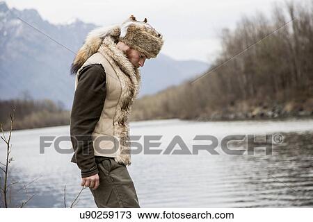 Stock Image - Mid adult man wearing trapper hat by river. Fotosearch