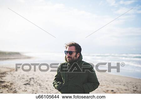 Picture - "Mid adult man with hands in pocket on breezy beach, Sorso, Sassari, Sardinia, Italy". Fotosearch