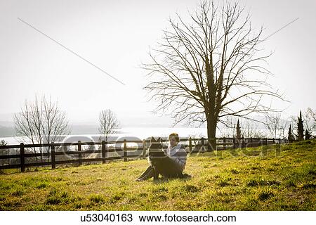 Mid adult woman and her dog sitting in lakeside field View Large Photo Image Stock Image - Mid adult woman and her dog sitting in lakeside field. Fotosearch