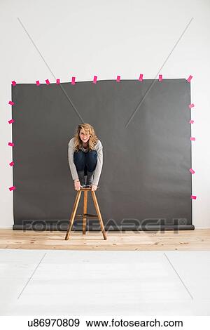 Stock Photo - Mid adult woman crouching on top of stool. Fotosearch