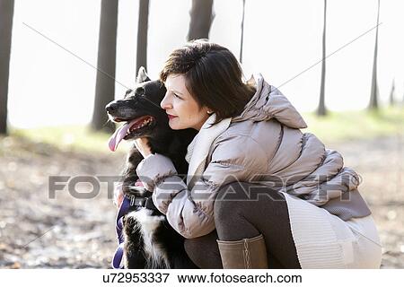 Stock Photo - Mid adult woman crouching with her dog on dirt path. Fotosearch
