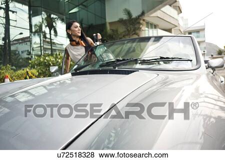 Stock Photo - Mid adult woman getting into convertible car. Fotosearch
