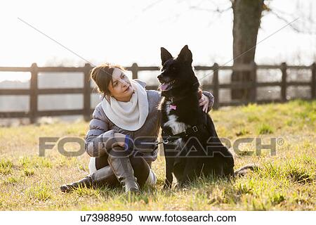 Mid adult woman sitting with her dog in field View Large Photo Image Stock Image - Mid adult woman sitting with her dog in field. Fotosearch