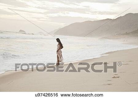 Stock Photograph - Mid adult woman walking along beach. Fotosearch