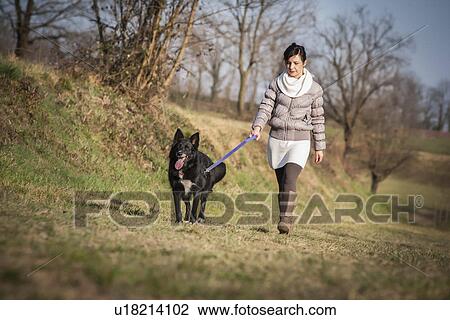 Stock Image - Mid adult woman walking her dog in field. Fotosearch