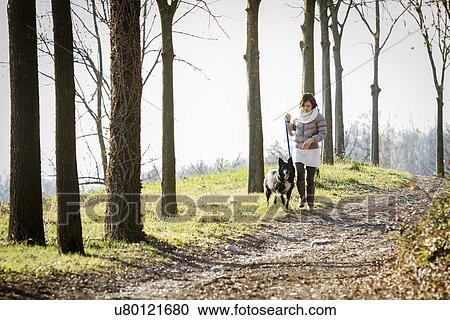 Stock Image - Mid adult woman walking her dog on dirt path. Fotosearch