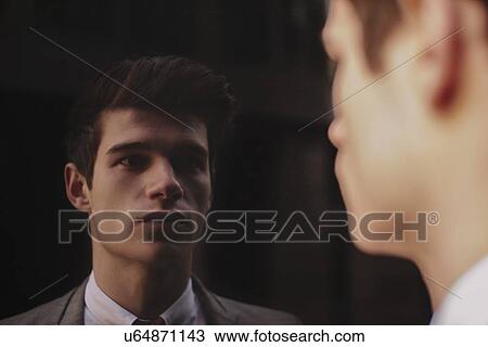 Stock Image - Mirror portrait of young businessman staring at dark tinted window. Fotosearch
