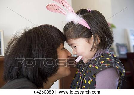 Stock Image - "Mother and daughter, face to face, daughter wearing bunny ears and holding sweet in her mouth". Fotosearch