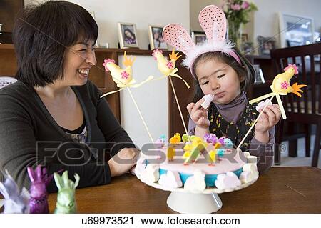 Stock Image - "Mother and daughter sitting at table, Easter cake in front of them". Fotosearch