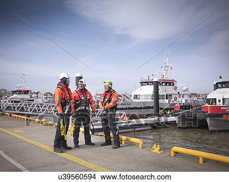 Picture - Offshore windfarm engineers on quayside with boats in the background. Fotosearch