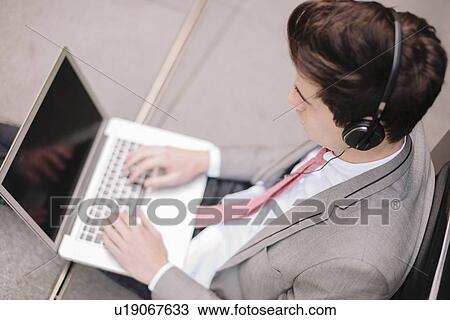 Over shoulder view of young city businessman sitting on sidewalk typing on laptop View Large Photo Image Stock Image - Over shoulder view of young city businessman sitting on sidewalk typing on laptop. Fotosearch