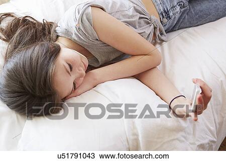 Overhead view of girl lying on bed reading smartphone text message View Large Photo Image Stock Image - Overhead view of girl lying on bed reading smartphone text message. Fotosearch