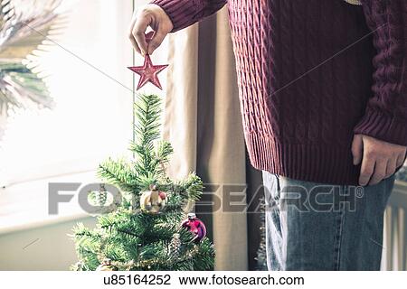 Stock Image - Person putting star on christmas tree. Fotosearch