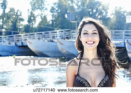 Stock Image - Portrait of a smiling young woman wearing a bikini standing in front of a river. Fotosearch